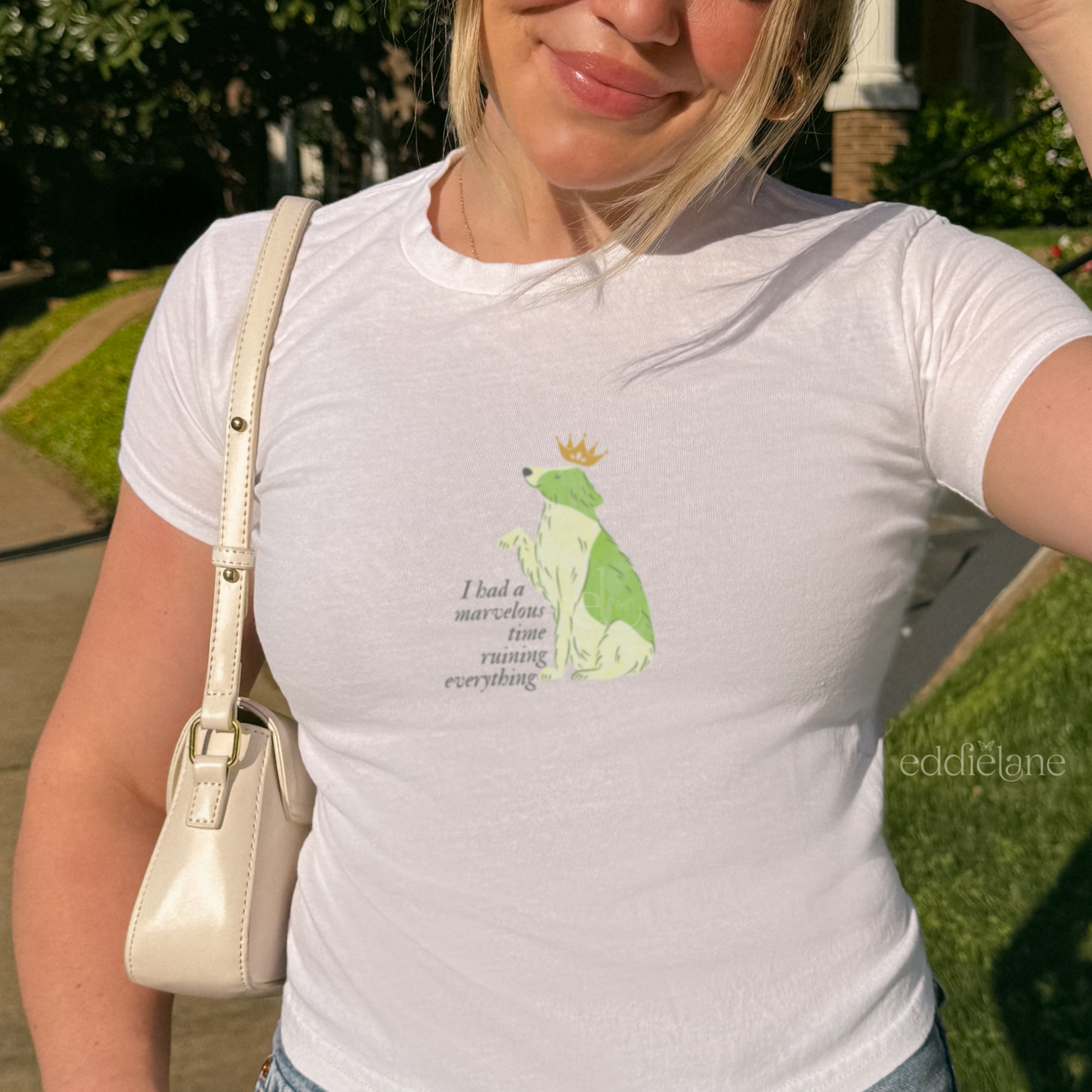 Girl wearing a black baby tee with a graphic of a key-lime green dog wearing a crown and the words "i had a marvelous time ruining everything", standing outdoors. Inspired by the song the last great american dynatsy from folklore by taylor swift.