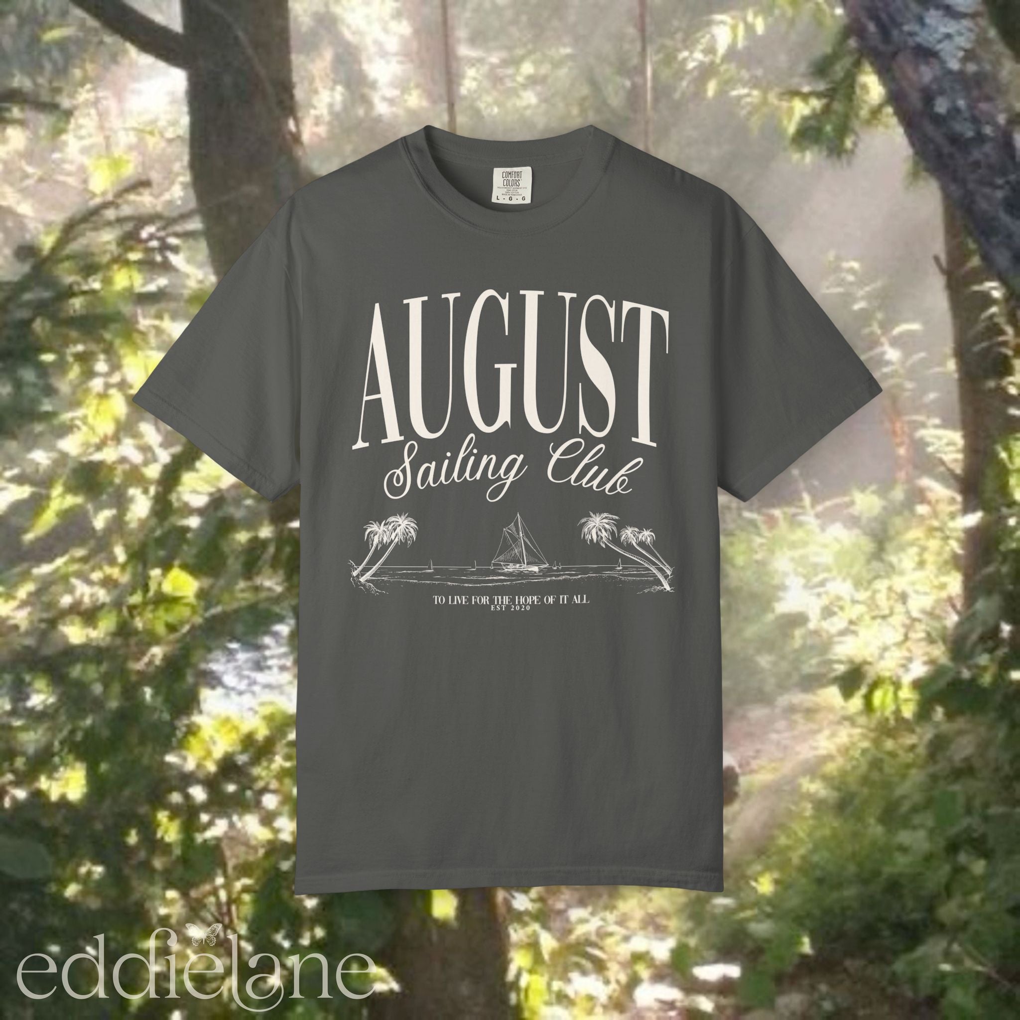 A minimalistic gray graphic tee that says 'August Sailing Club' with a sketch design of sailboats on a beach. 
