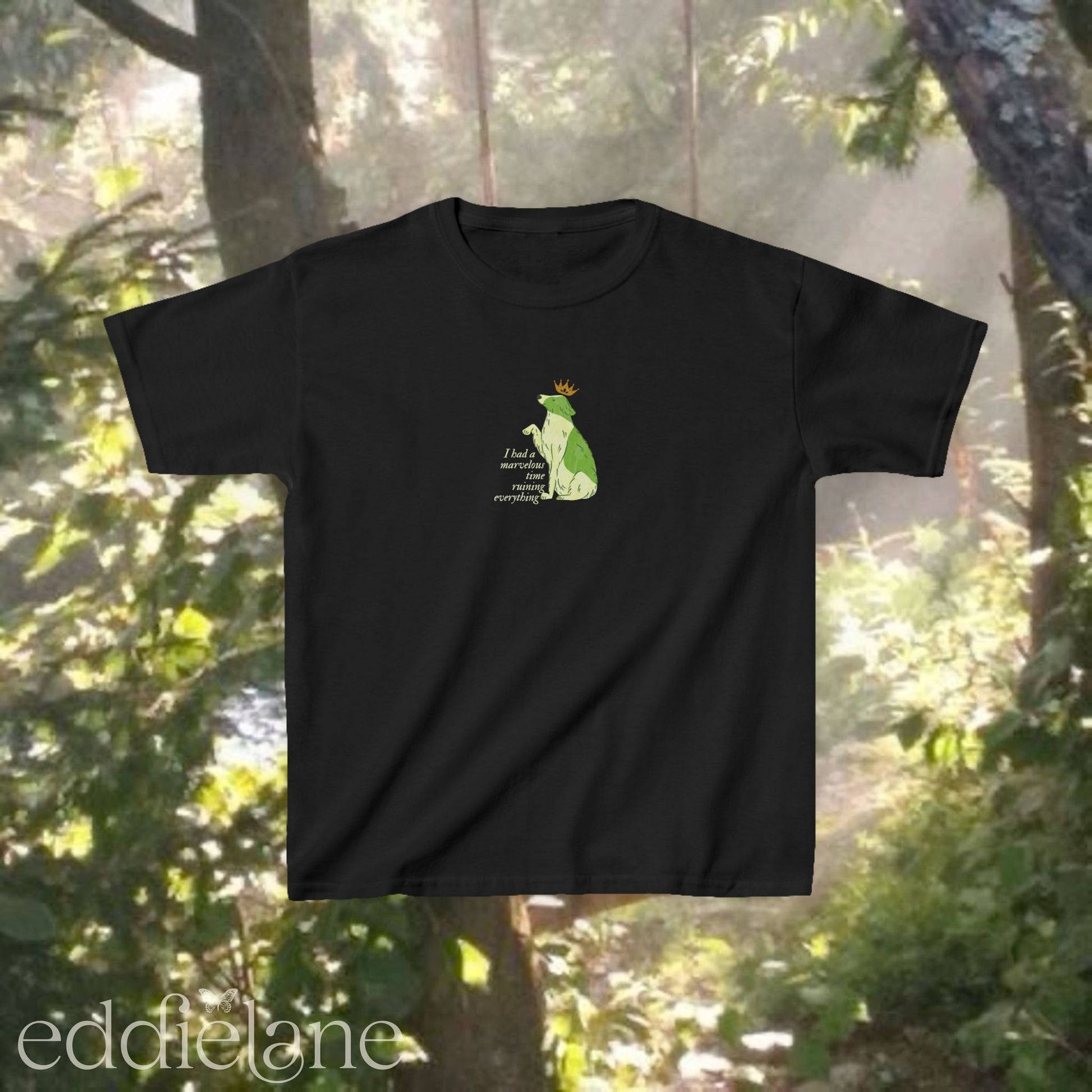 A black baby tee with a graphic of a key-lime green dog wearing a crown and the words "i had a marvelous time ruining everything". Inspired by the song the last great american dynatsy from folklore by taylor swift.