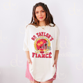 Woman wearing an ivory oversized t-shirt with a vintage football helmet design and text that says "go taylor's fiance"