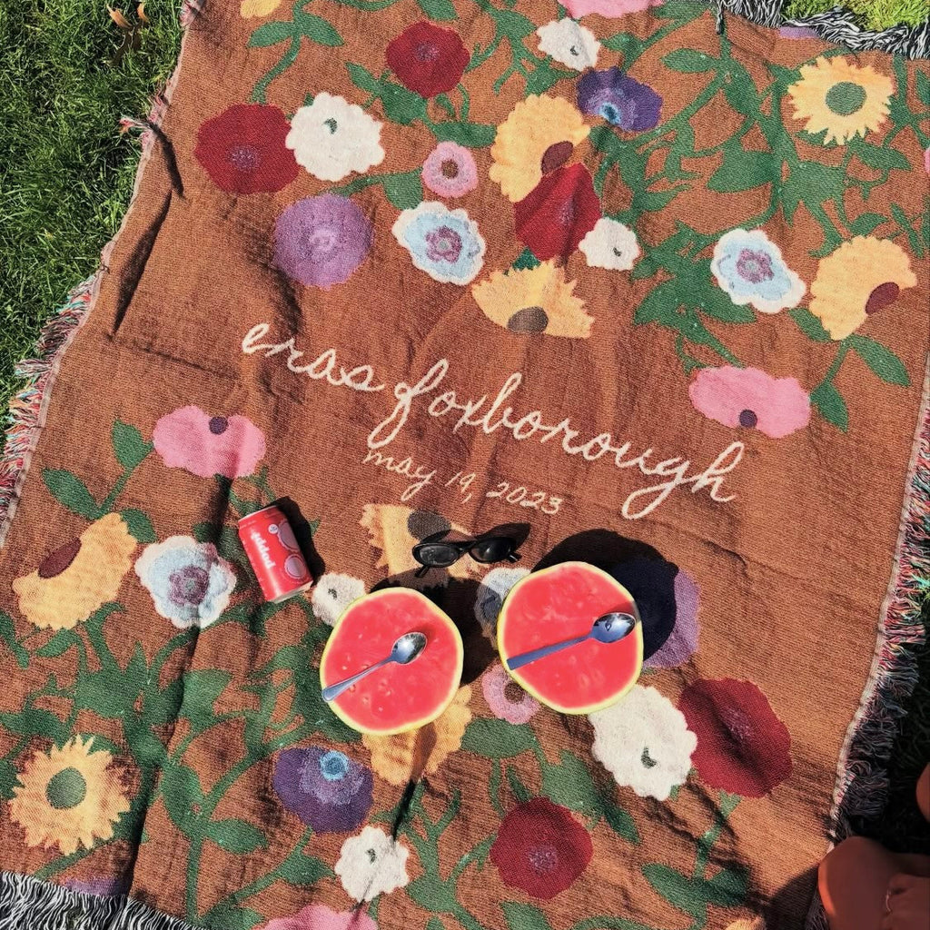 Floral-patterned blanket with text and small figures on a grassy background