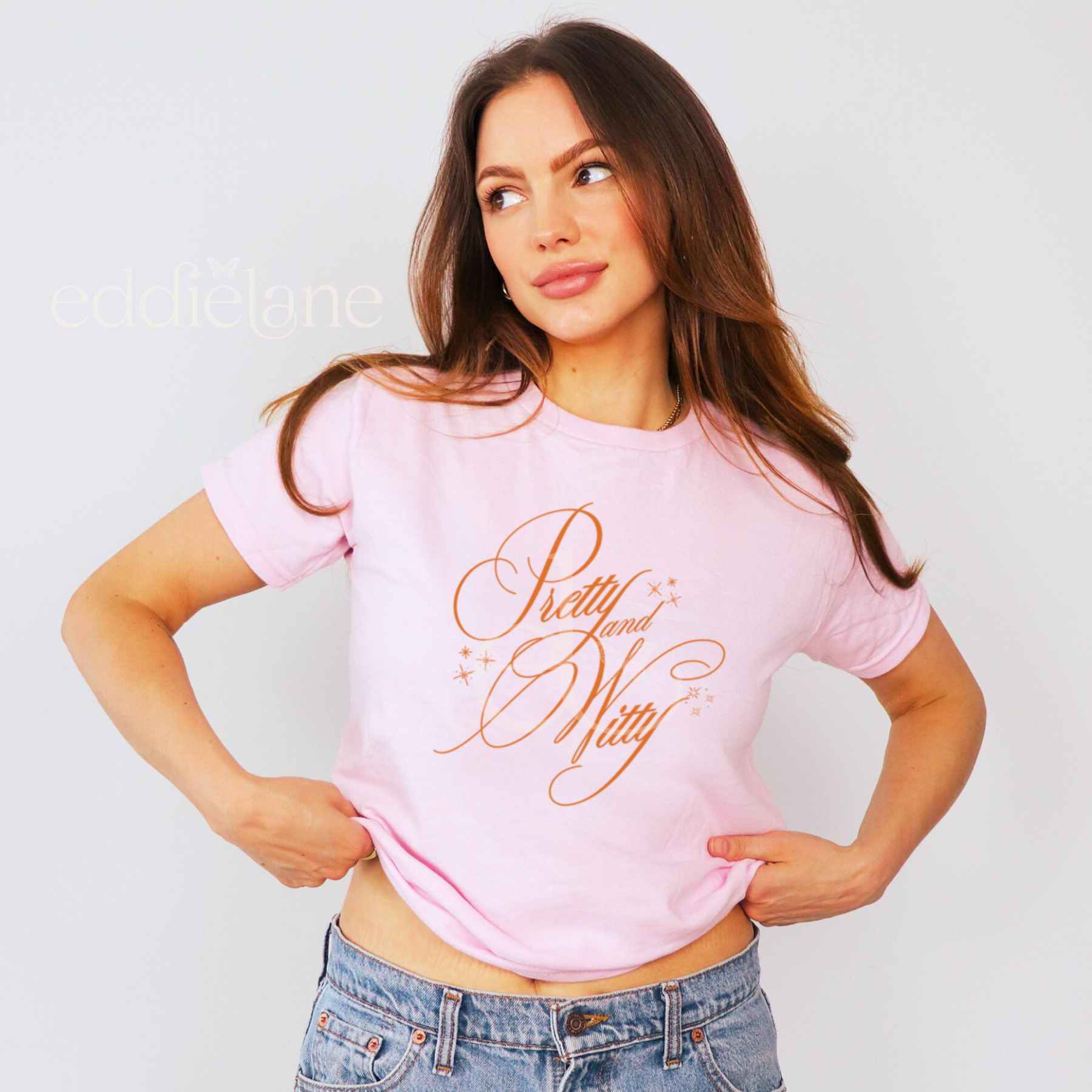 woman wearing a pink baby tee that says "pretty and witty" in a vintage style script font