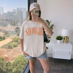 Woman wearing a comfort colors graphic tee that says 'SHOWGIRL' with two small stars