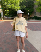 Girl wearing a yellow graphic t-shirt with 'Holiday House Bed & Breakfast' design, 
banana comfort colors shirt