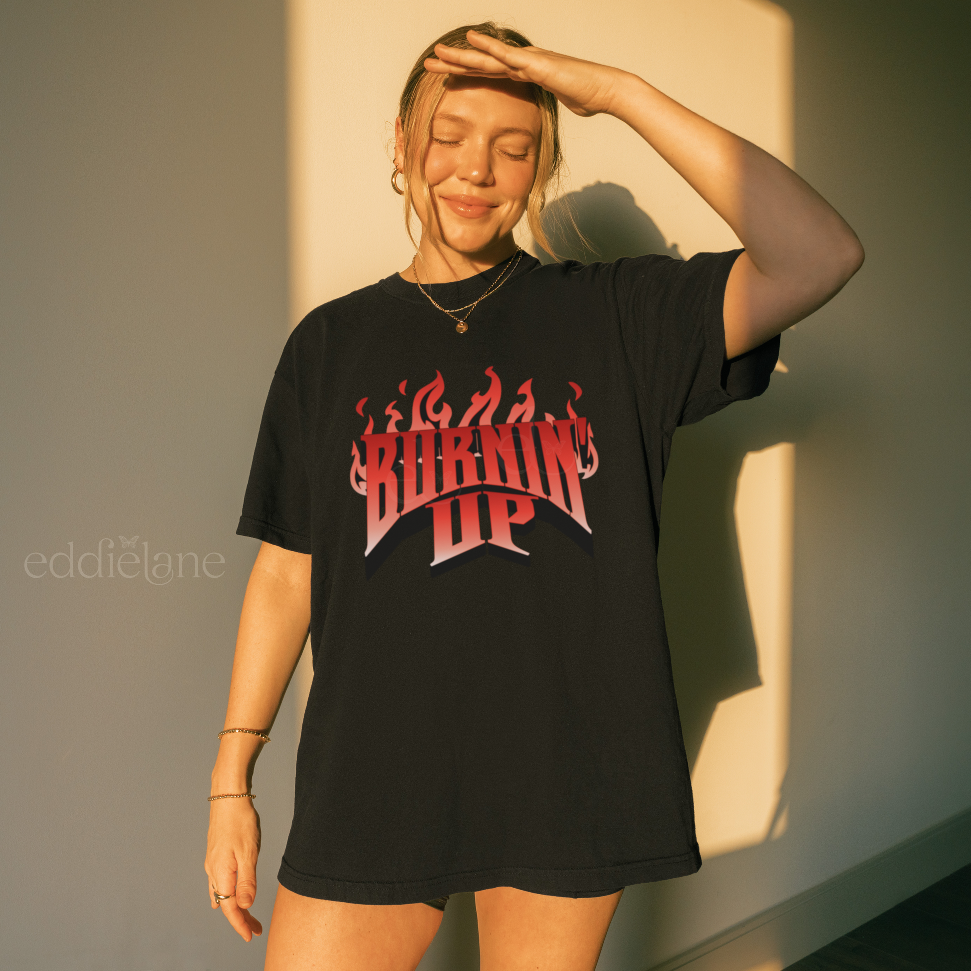 Woman wearing an oversized black t-shirt with red and white graphic design that says "BURNIN' UP" in front of flames inspired by the Jonas Brothers.