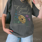 Person wearing a gray graphic tee with a floral design that says 'Charlie's Garden' t-shirt with floral design,