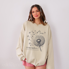 Woman wearing a beige sweatshirt with a dandelion graphic and text that says "do you remember" 
