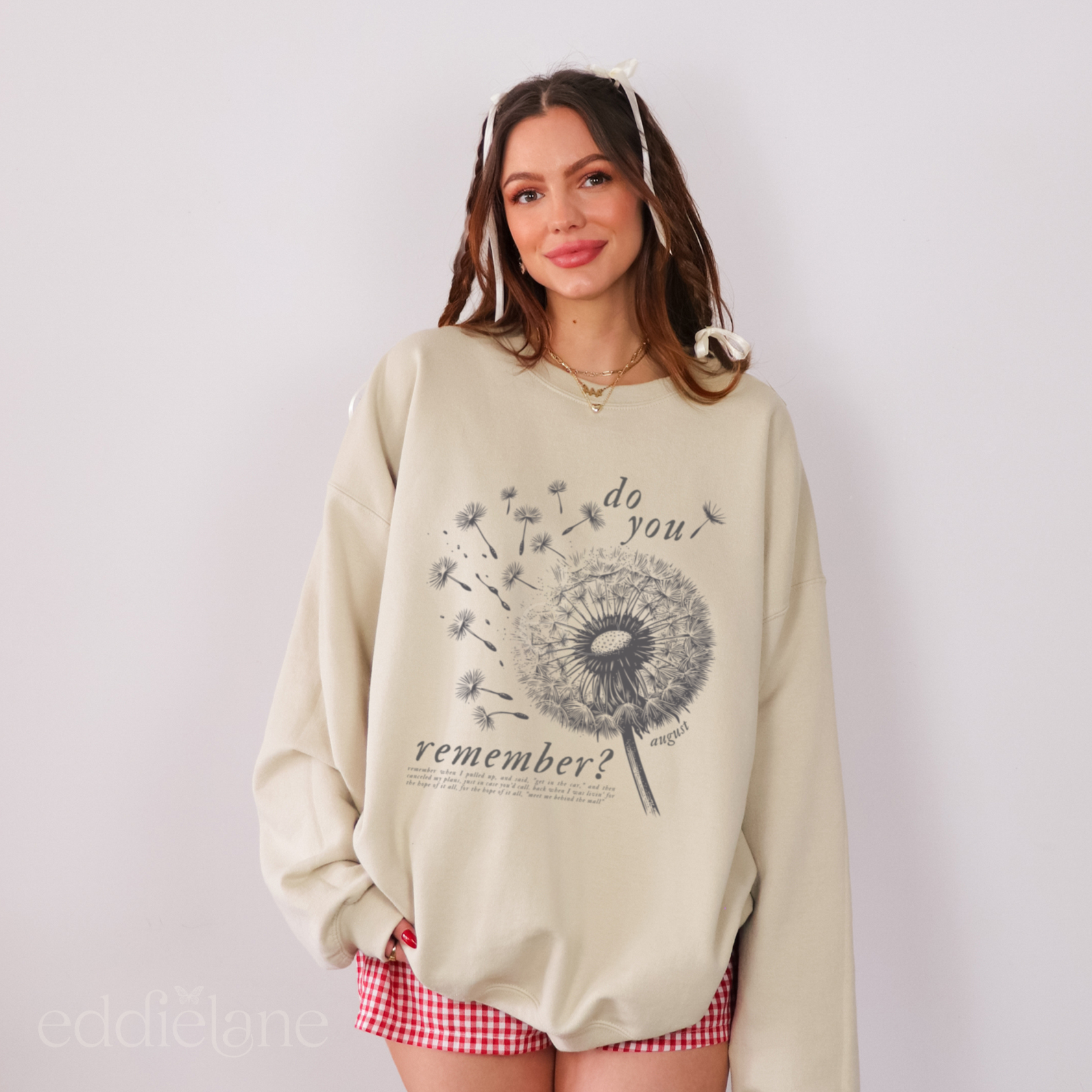 Woman wearing a beige sweatshirt with a dandelion graphic and text that says "do you remember" 