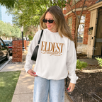 Woman wearing a white sweatshirt that says 'Eldest Daughter social club'.