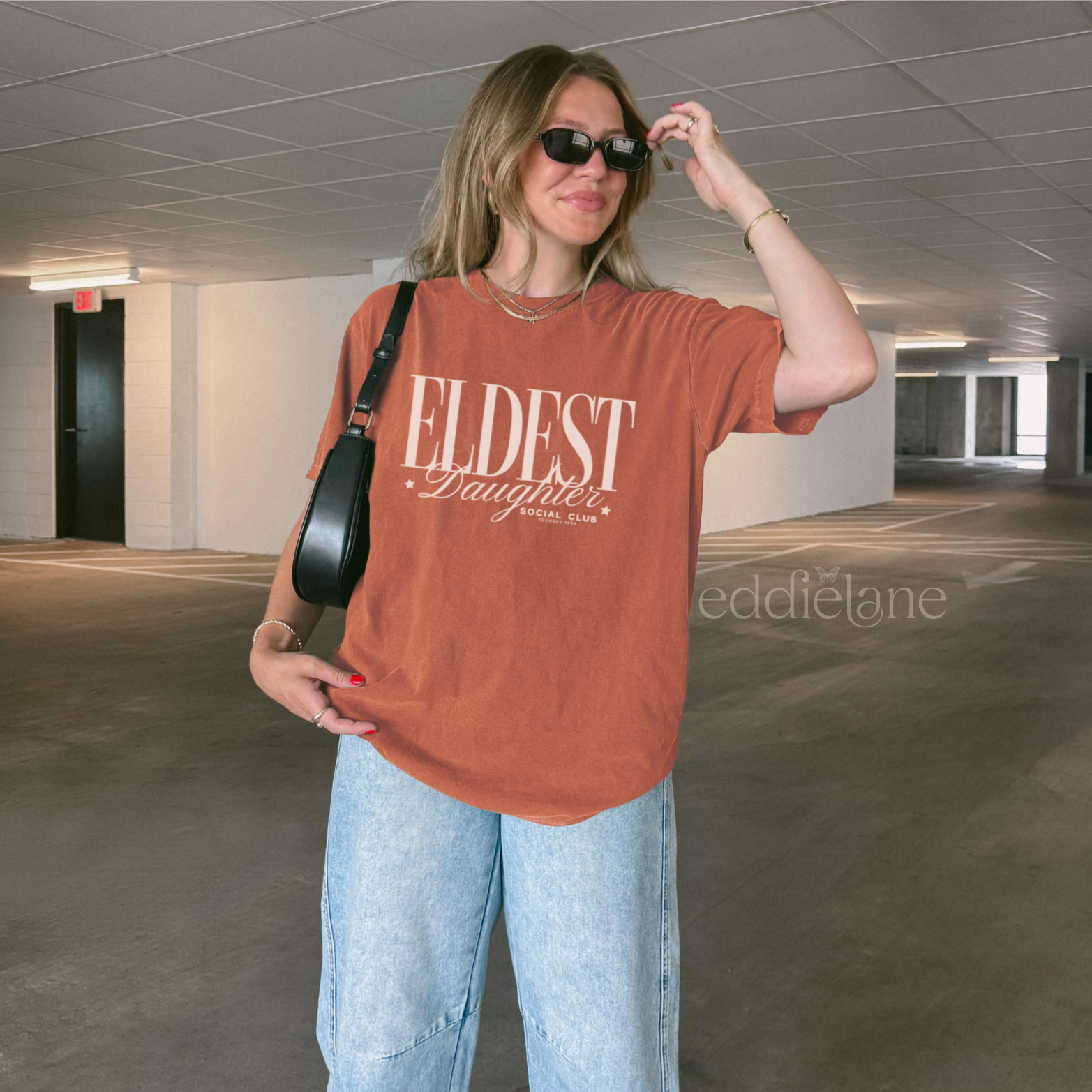 woman wearing an orange t-shirt that says "eldest daughter social club"