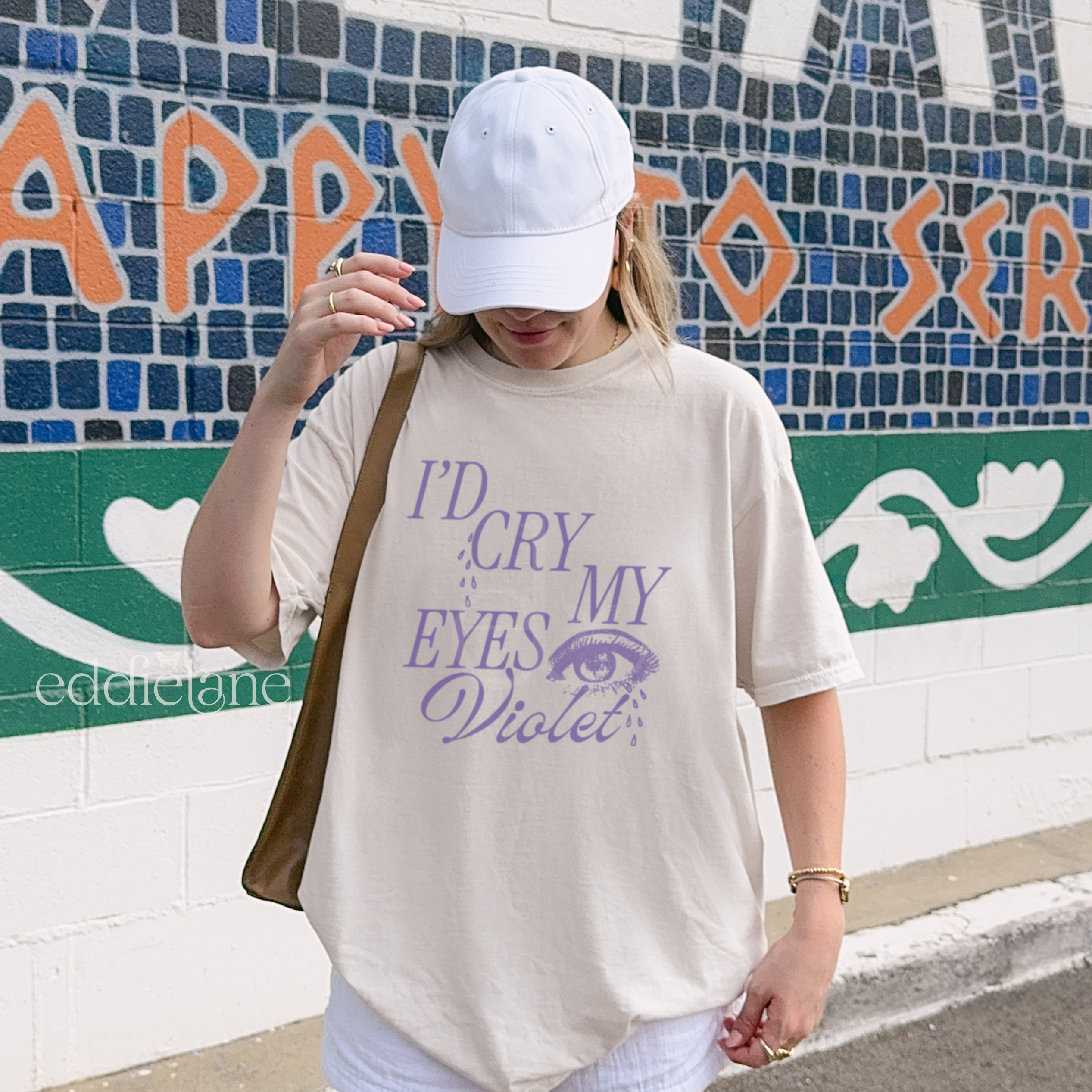 Person wearing a beige oversized t-shirt with the words "I'd cry my eyes violet"