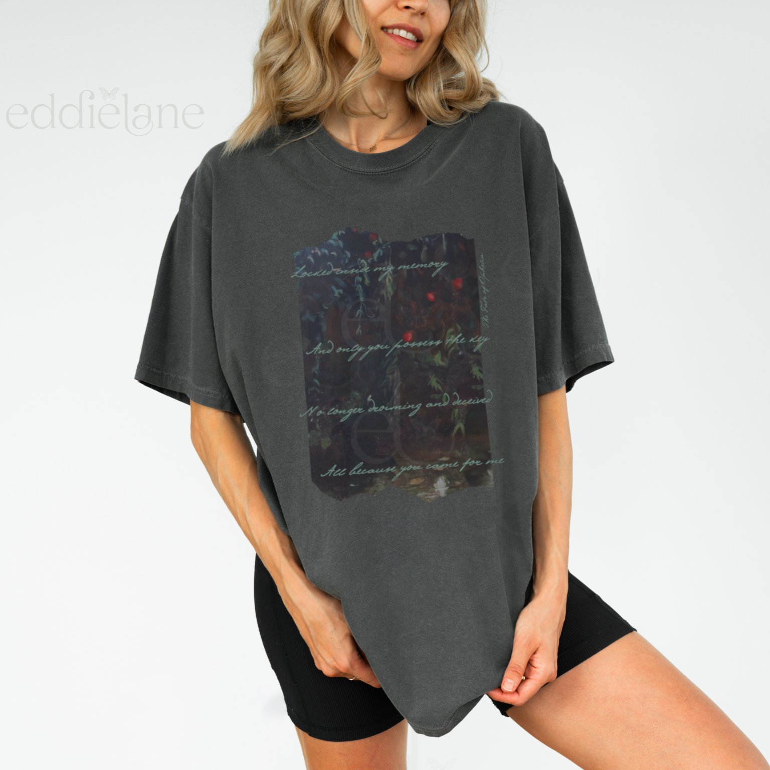 Woman wearing a dark gray t-shirt with a picutre of a painting and the words "Locked inside my memory and only you possess the key no longer drowning and deceived all because you came for me"