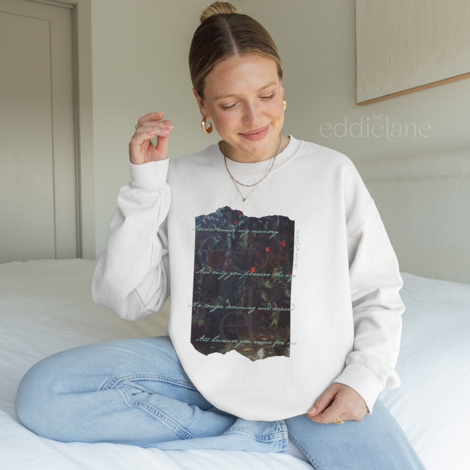 Woman wearing a white sweatshirt with a picutre of a painting and the words "Locked inside my memory and only you possess the key no longer drowning and deceived all because you came for me"