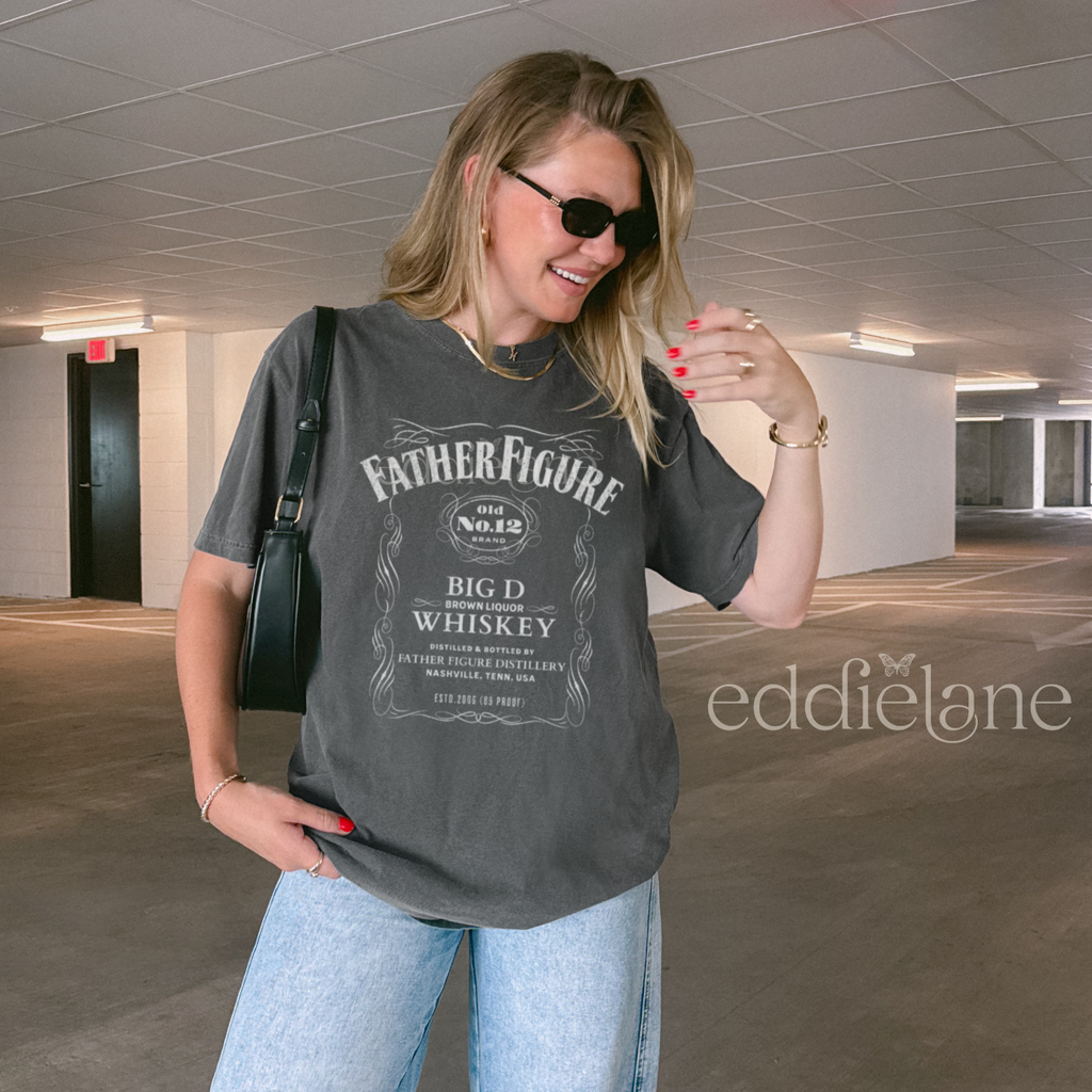 Woman wearing a 'Father Figure Whiskey' graphic t-shirt 