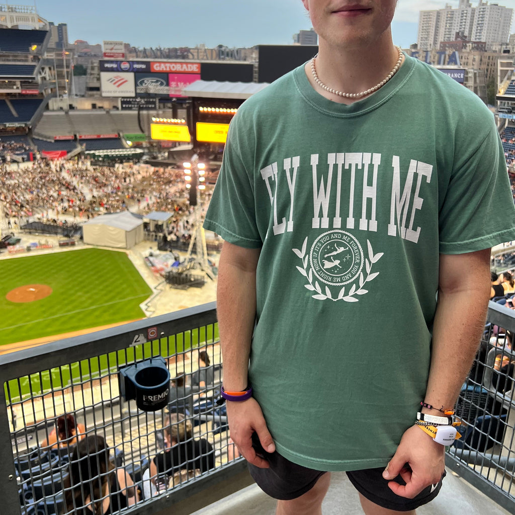 Man wearing a green 'Fly With Me' collegiate t-shirt 
