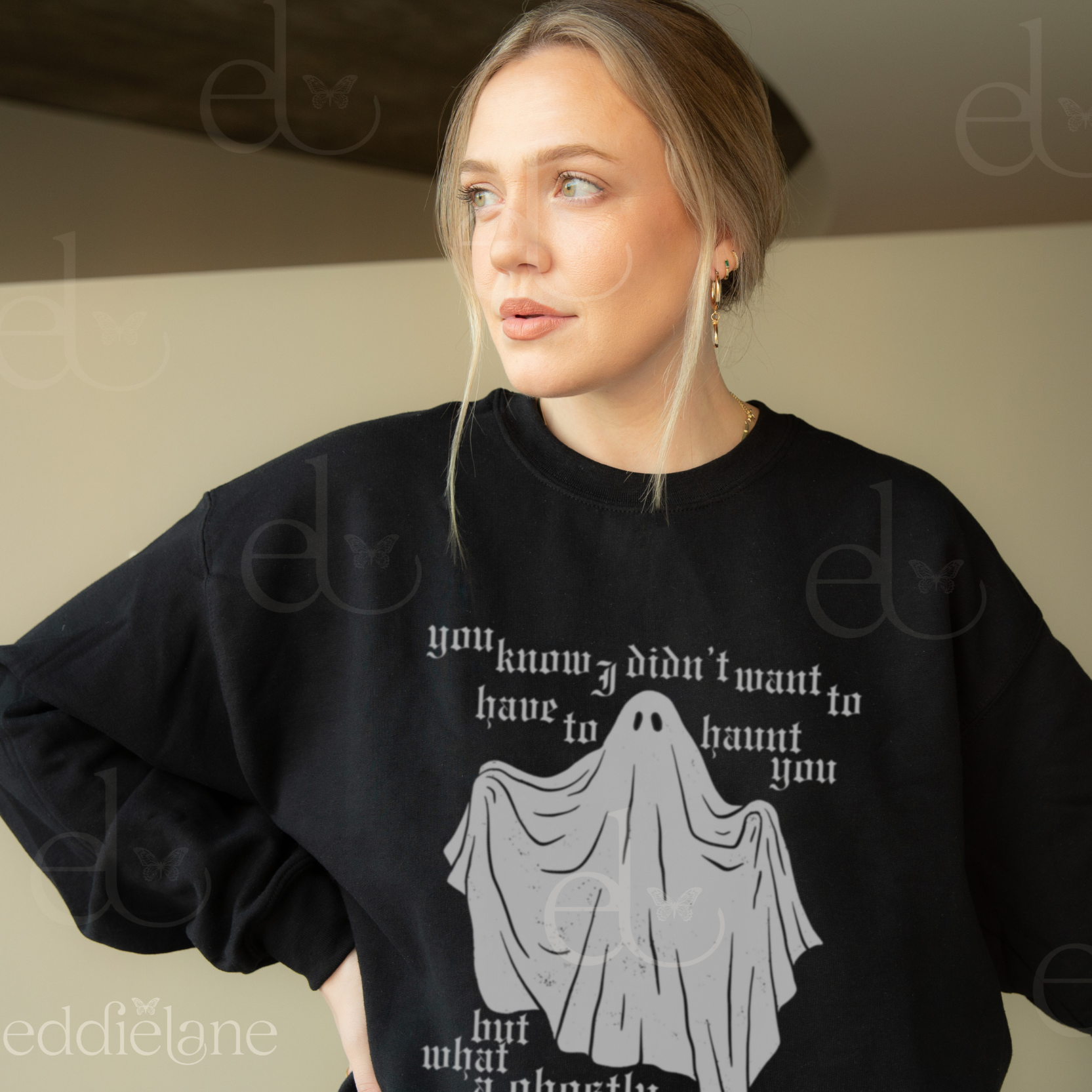Woman wearing a black sweatshirt with a ghost graphic and text, standing against a plain background.