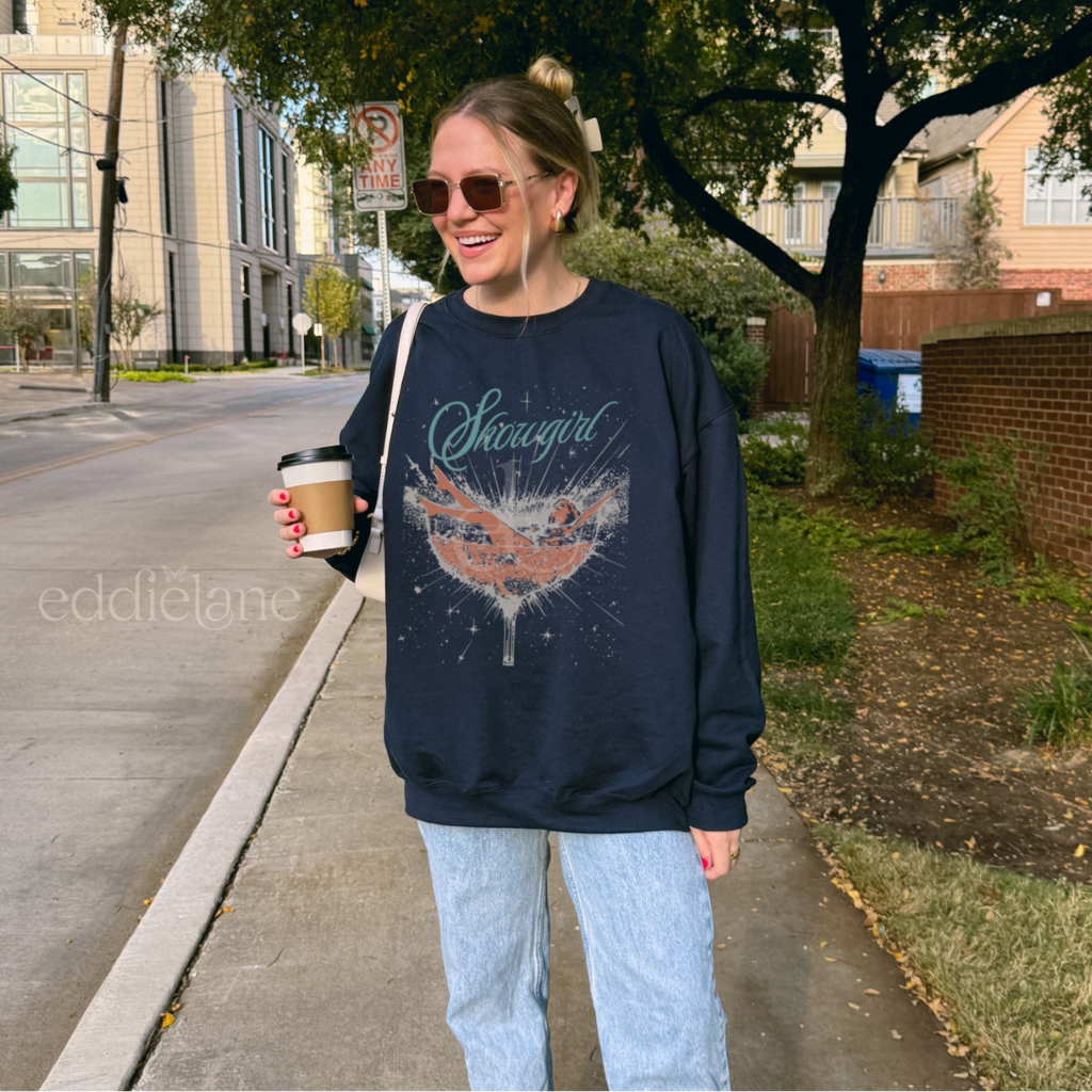 Woman wearing a navy sweatshirt with a graphic design of a woman in a martini glass and the word "showgirl"