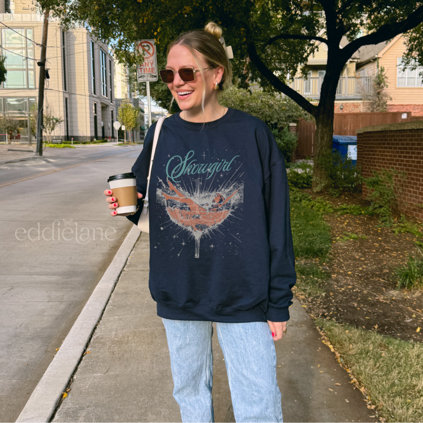 Woman wearing a navy sweatshirt with a graphic design of a woman in a martini glass and the word "showgirl"