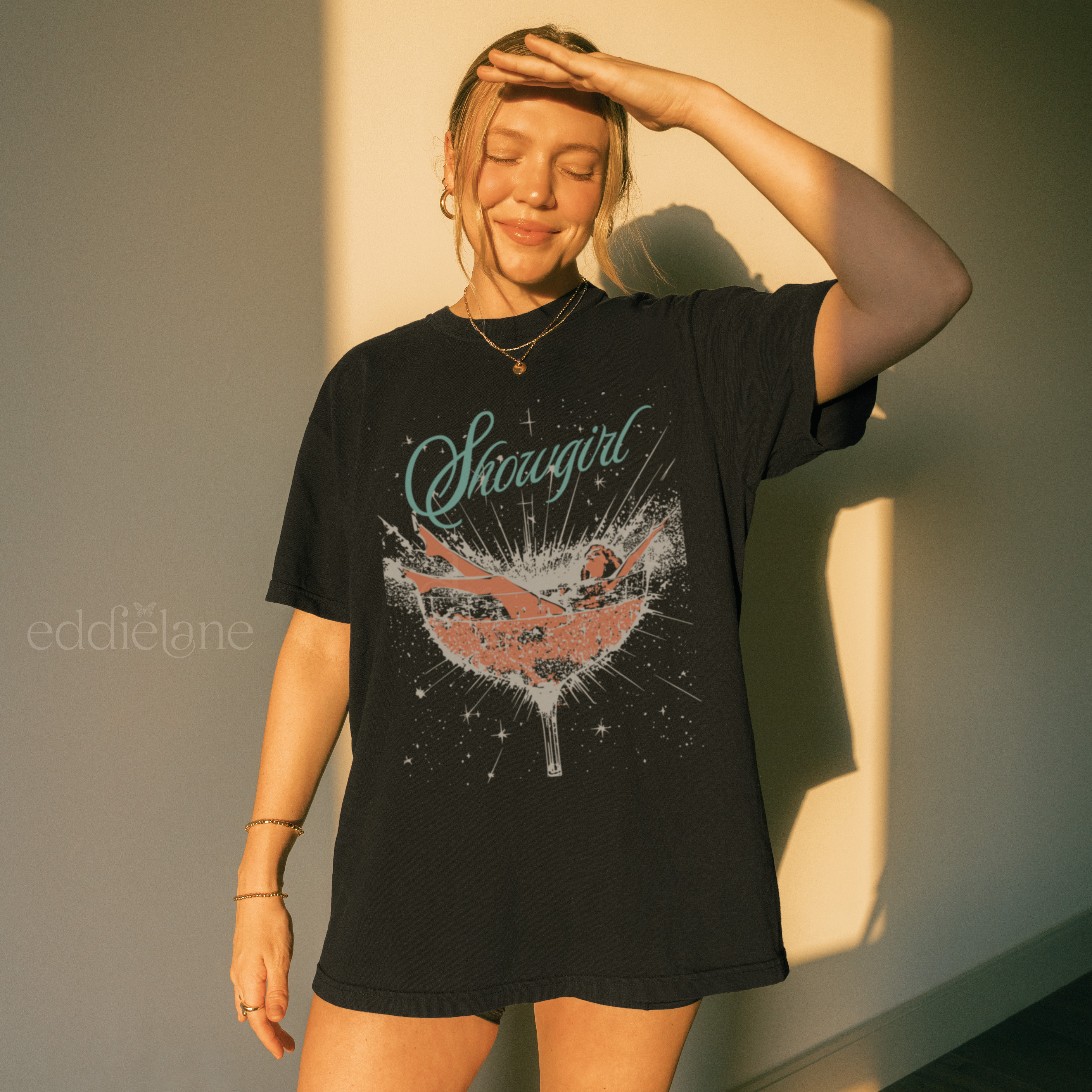woman wearing an oversized black t-shirt featuring a graphic of a woman in a champagne glass surrounded by sparkles