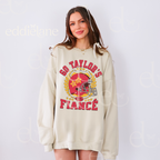 woman wearing an oversized sand crewneck sweatshirt with a vintage football helmet design and text that says "go taylor's fiance"