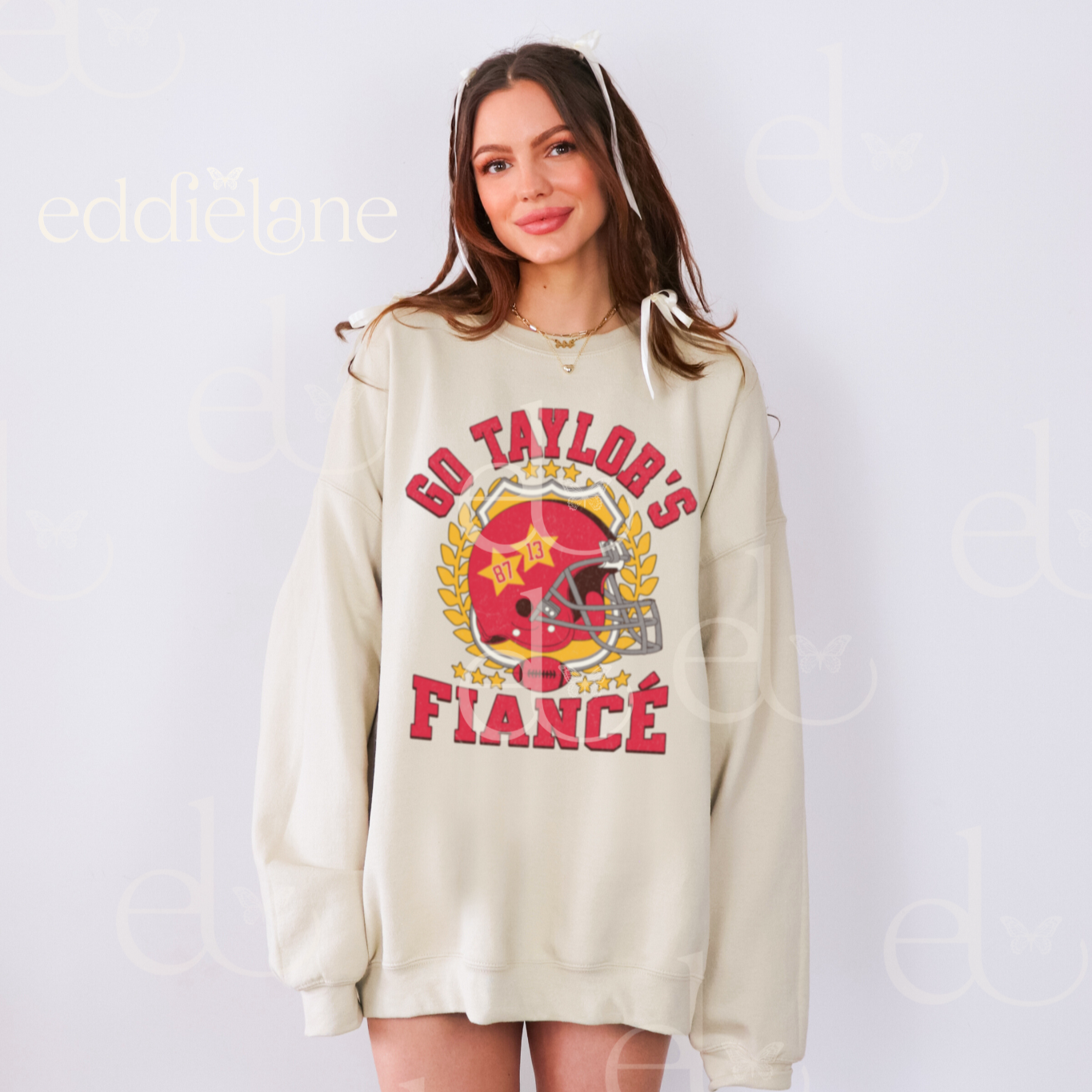 woman wearing an oversized sand crewneck sweatshirt with a vintage football helmet design and text that says "go taylor's fiance"