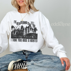 Woman wearing a white sweatshirt with a graphic design of haunted mansion and text "i think your house is haunted".