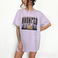 woman wearing an oversized light purple graphic tee that says "can't turn back now i'm haunted" with a graphic of spooky trees and a bell