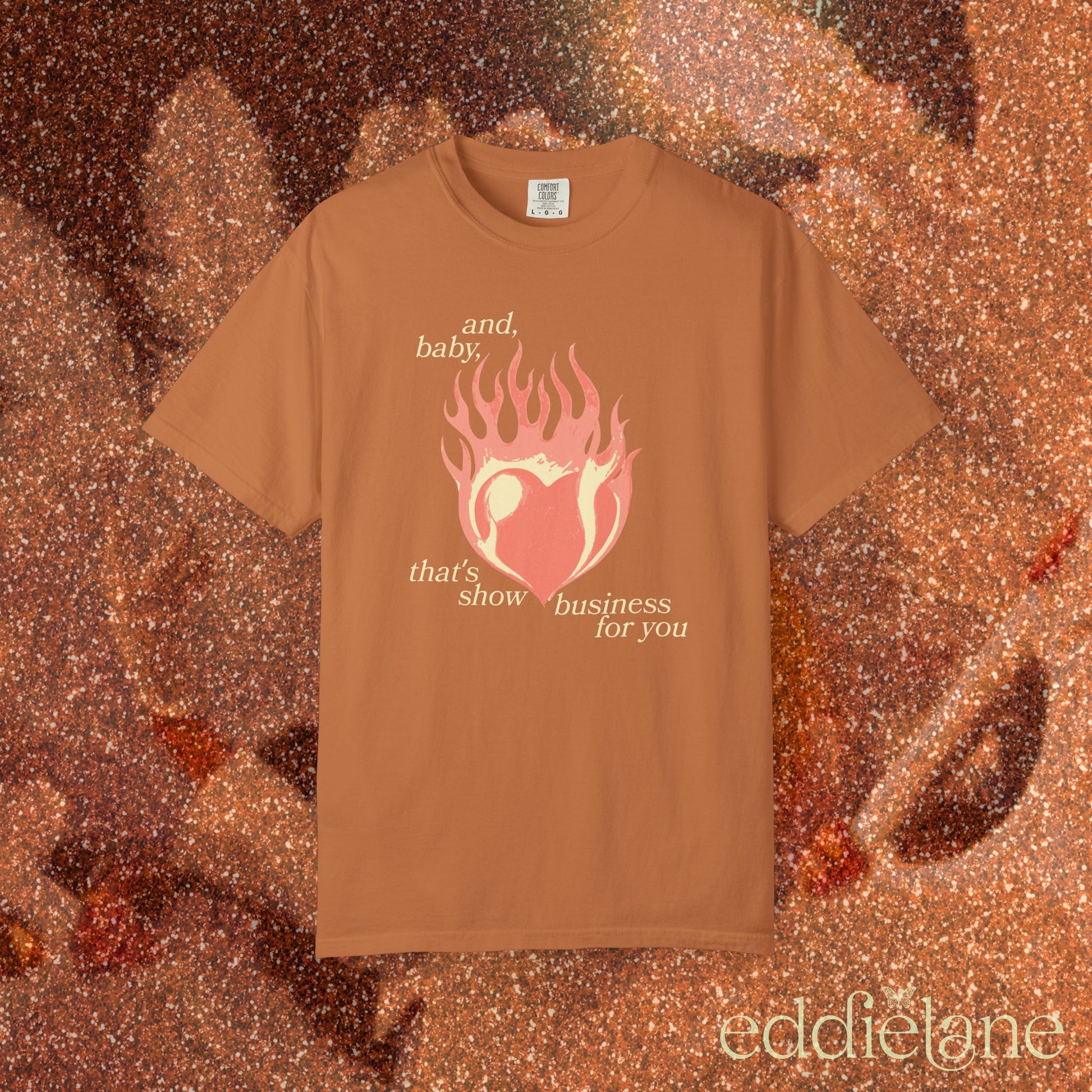 a burnt orange t-shirt with a heart in flames graphic and the words "and, baby, that's show business for you" inspired by taylor swift.
heart on fire yam