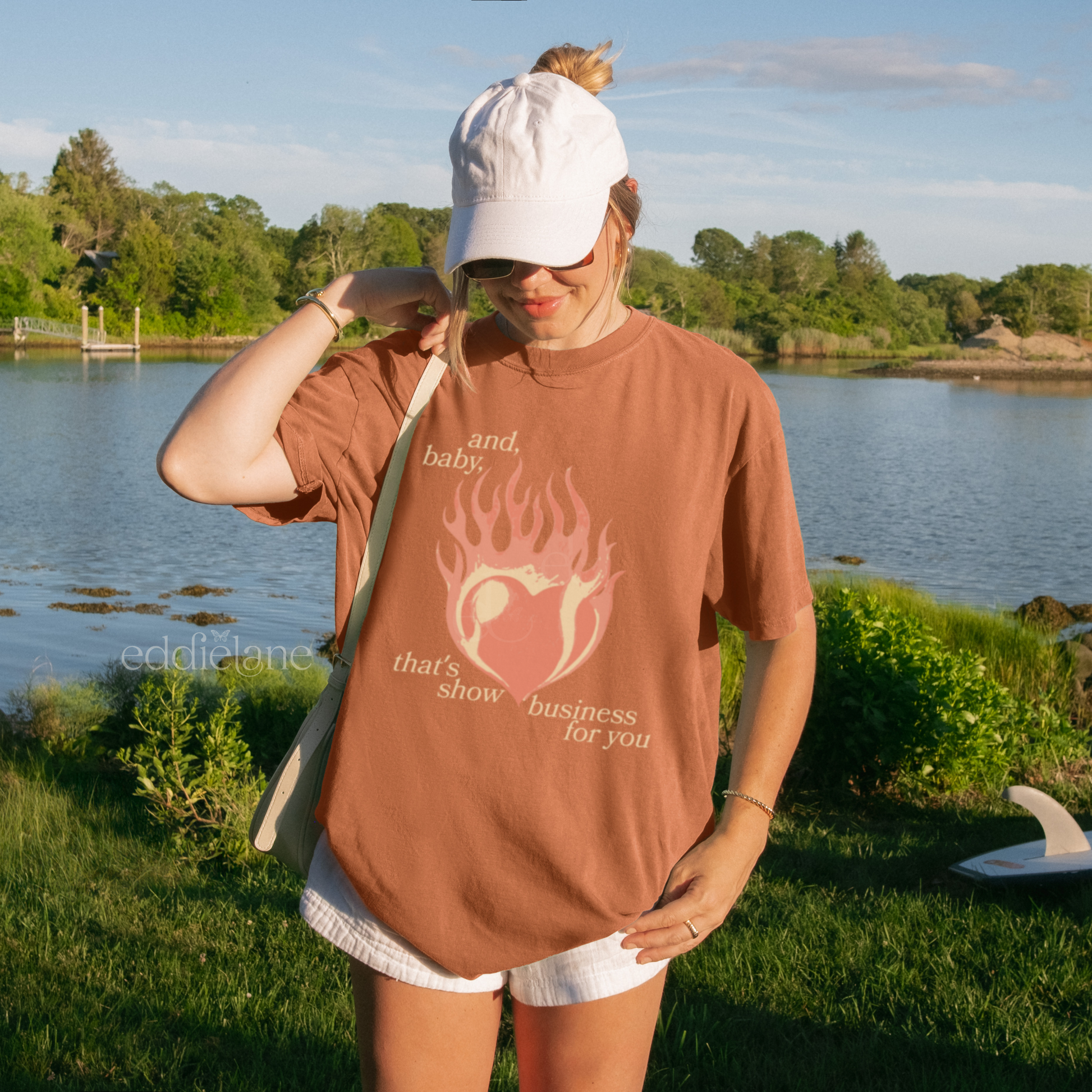 Woman wearing a burnt orange t-shirt with a heart in flames graphic and the words "and, baby, that's show business for you" inspired by taylor swift.
