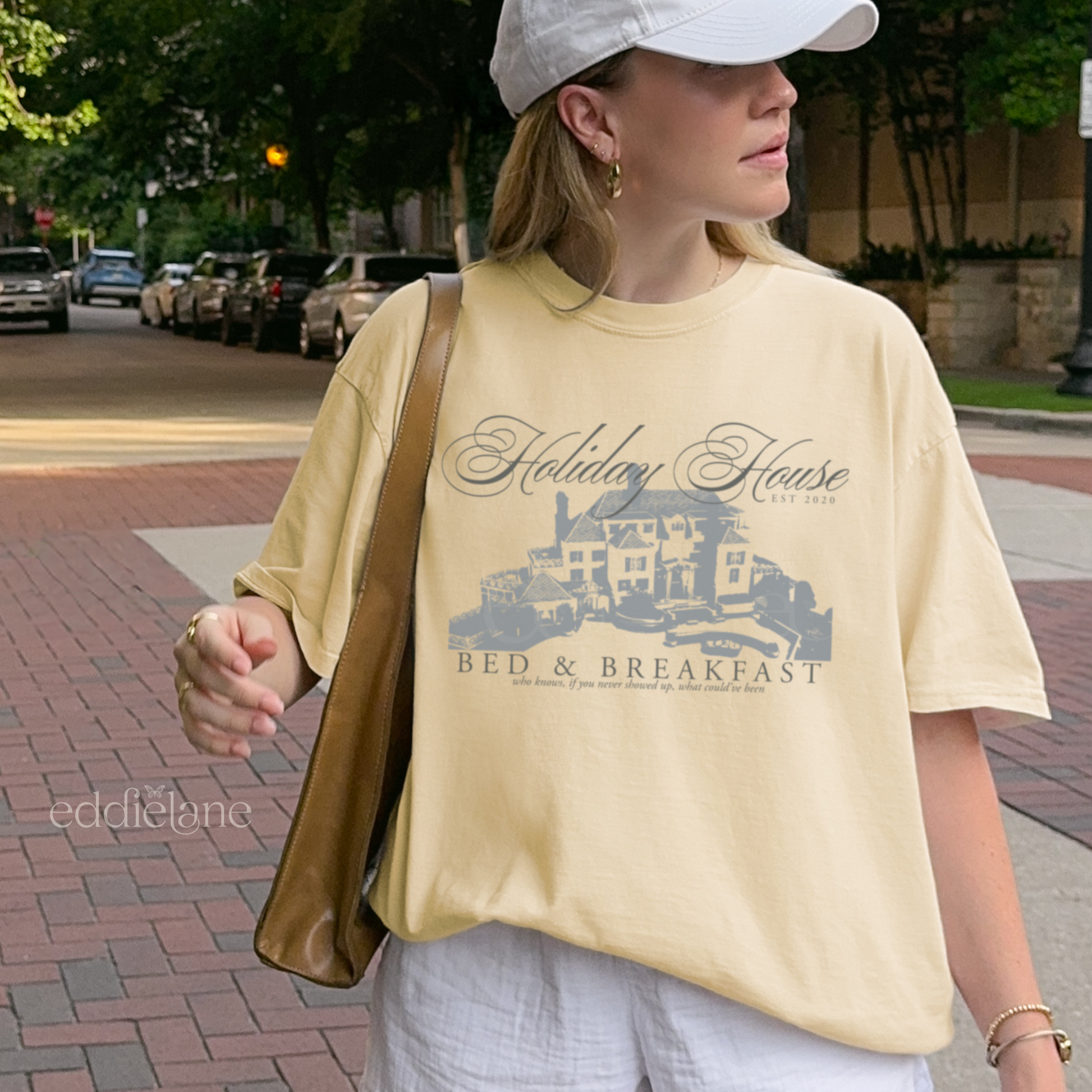 Girl wearing a yellow graphic t-shirt with 'Holiday House Bed & Breakfast' design, inspired by the last great american dynasty from folklore by taylor swift.