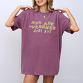 A woman in a berry-colored comfort colors oversized t-shirt that says "hugs are overrated just fyi" 
