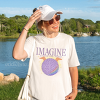 Woman wearing a 'Imagine Around the World' white comfort colors tshirt with a graphic of a figment inspired epcot ball