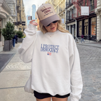 Woman wearing a white sweatshirt with 'I Protect Democracy' text above an upside down american flag