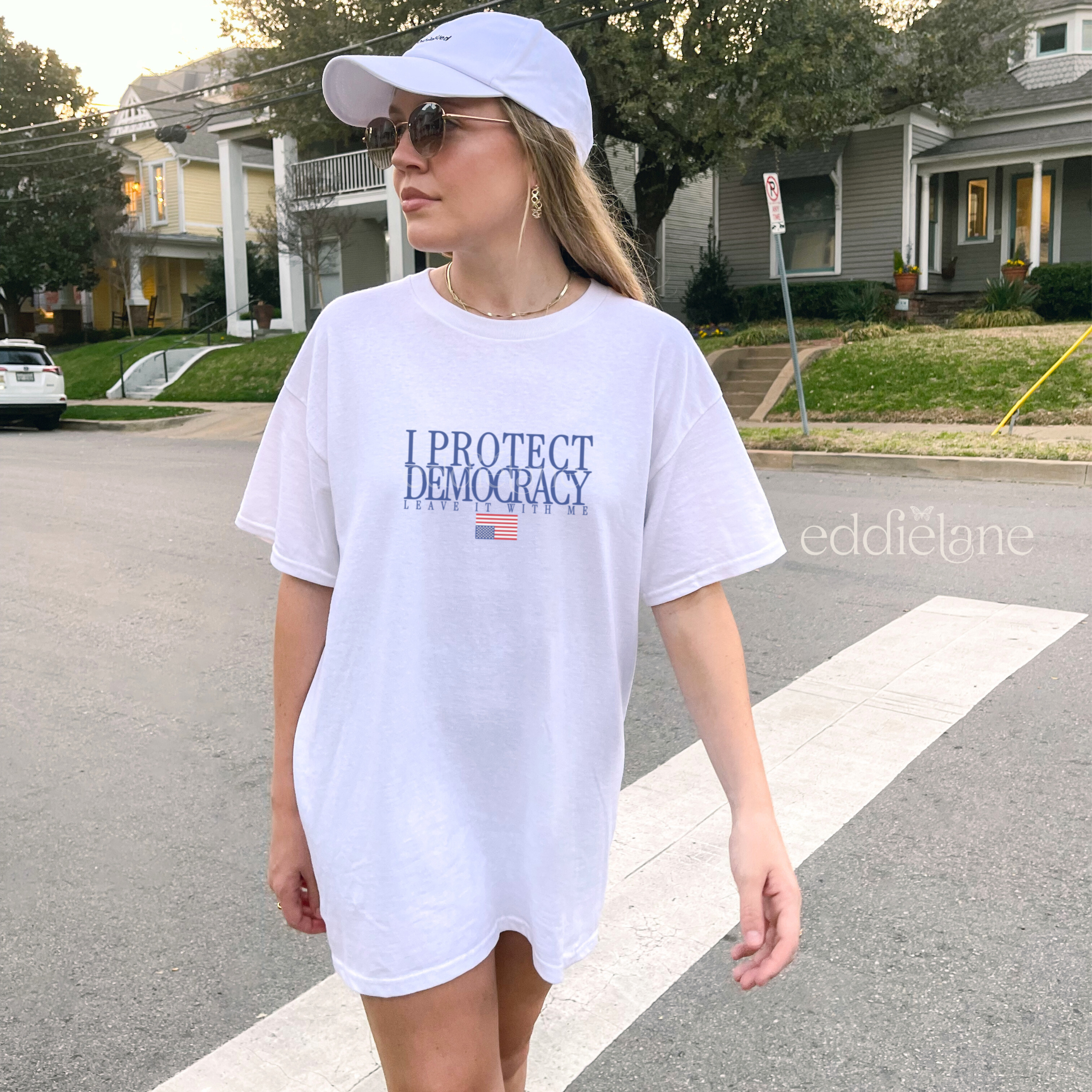 Woman wearing a white comfort colors t-shirt with 'I Protect Democracy' above an upside down american flag