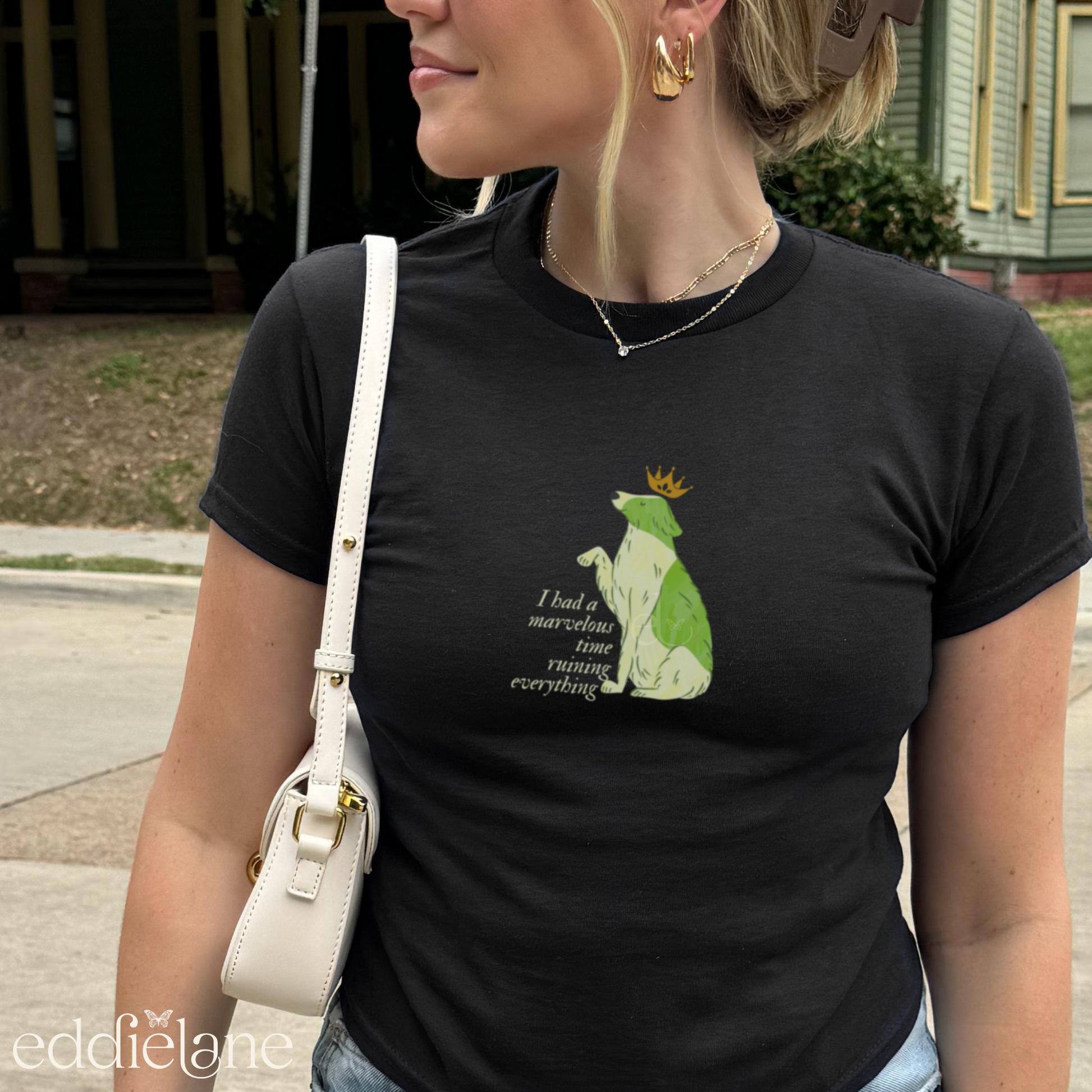 Girl wearing a black baby tee with a graphic of a key-lime green dog wearing a crown and the words "i had a marvelous time ruining everything", standing outdoors. Inspired by the song the last great american dynatsy from folklore by taylor swift.