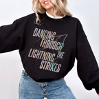 Woman wearing a black sweatshirt with the words "dancing through the lightning strikes" and a colorful lightning bolt design