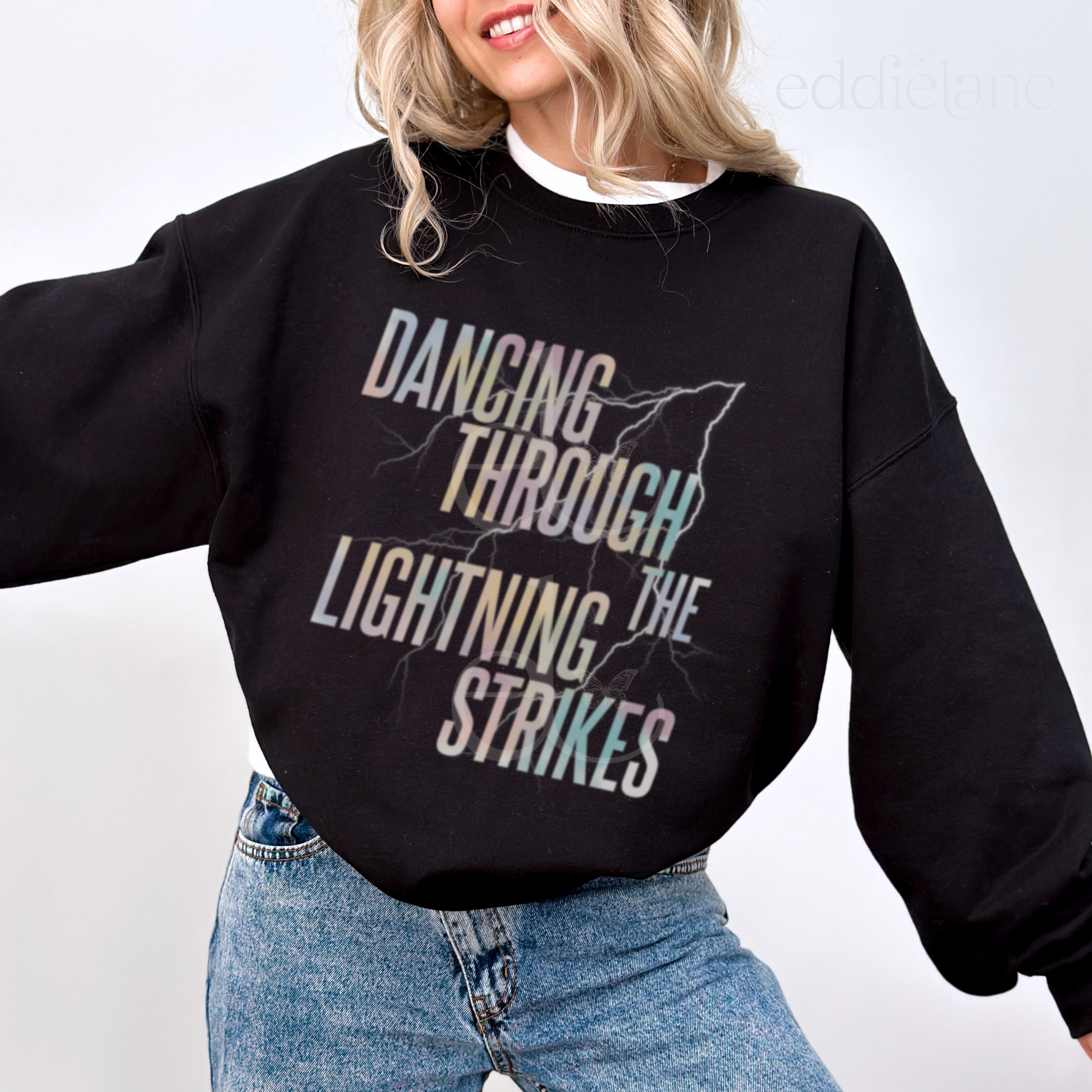 Woman wearing a black sweatshirt with the words "dancing through the lightning strikes" and a colorful lightning bolt design