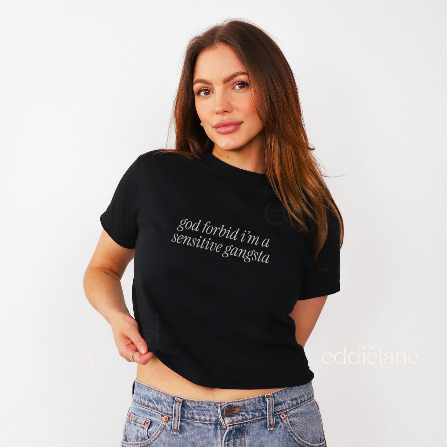 Woman wearing a black baby tee that says "god forbid i'm a sensitive gangsta" inspired by amaya from love island usa.