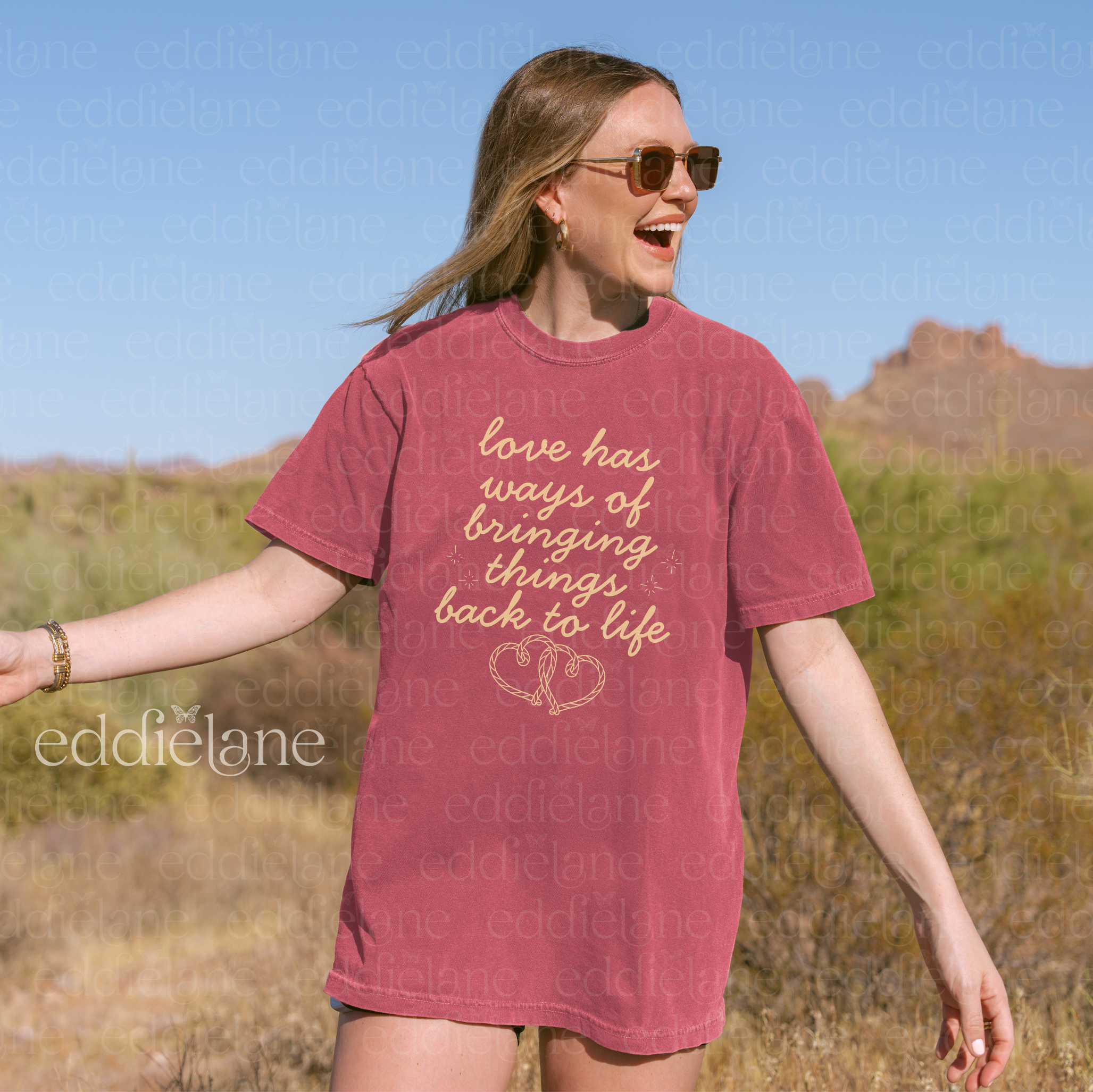 Woman wearing a red t-shirt with text and a heart design, standing in a desert landscape.