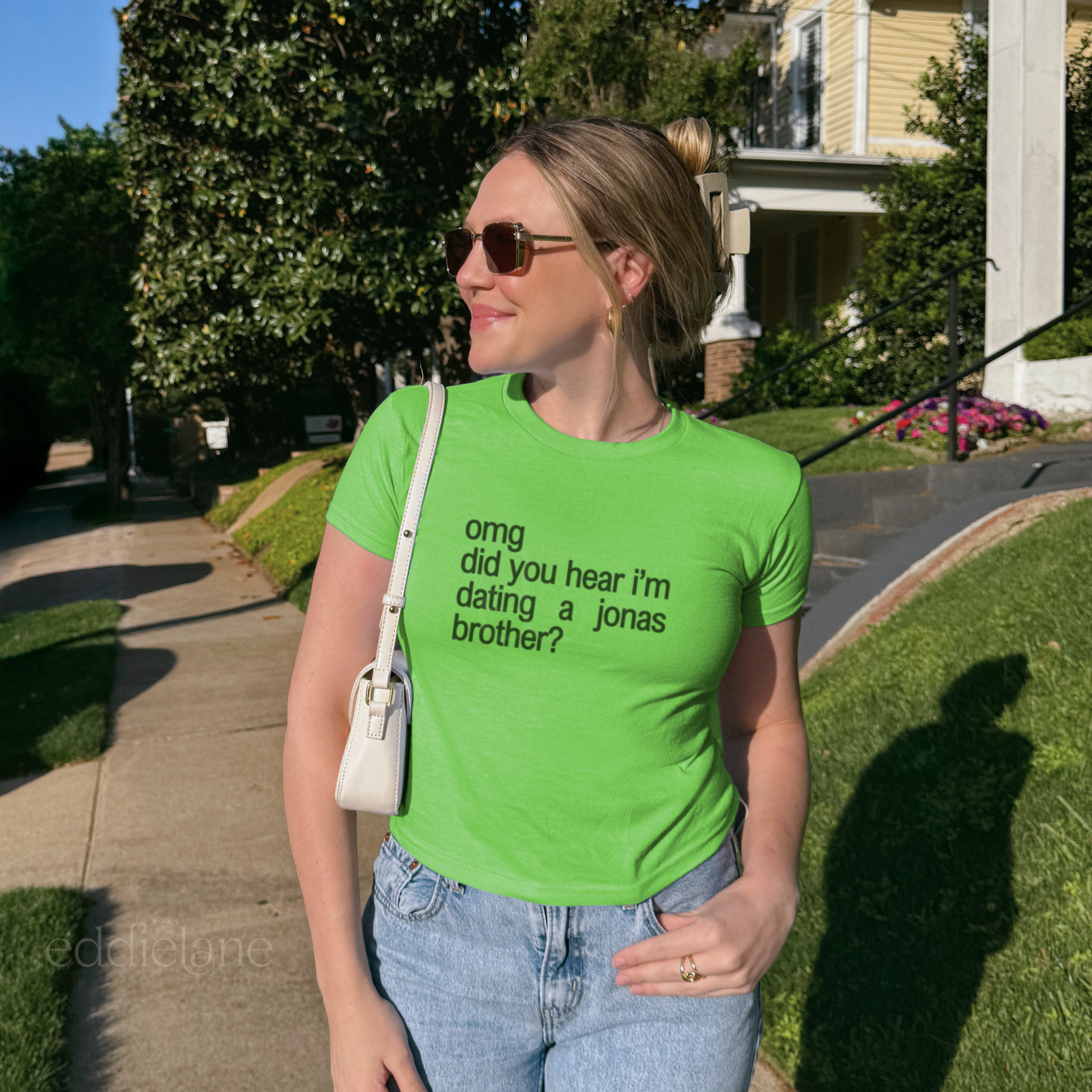 Woman wearing a brat green baby tee that says "omg did you hear i'm dating a jonas brother?" from video girl by the jonas brothers.