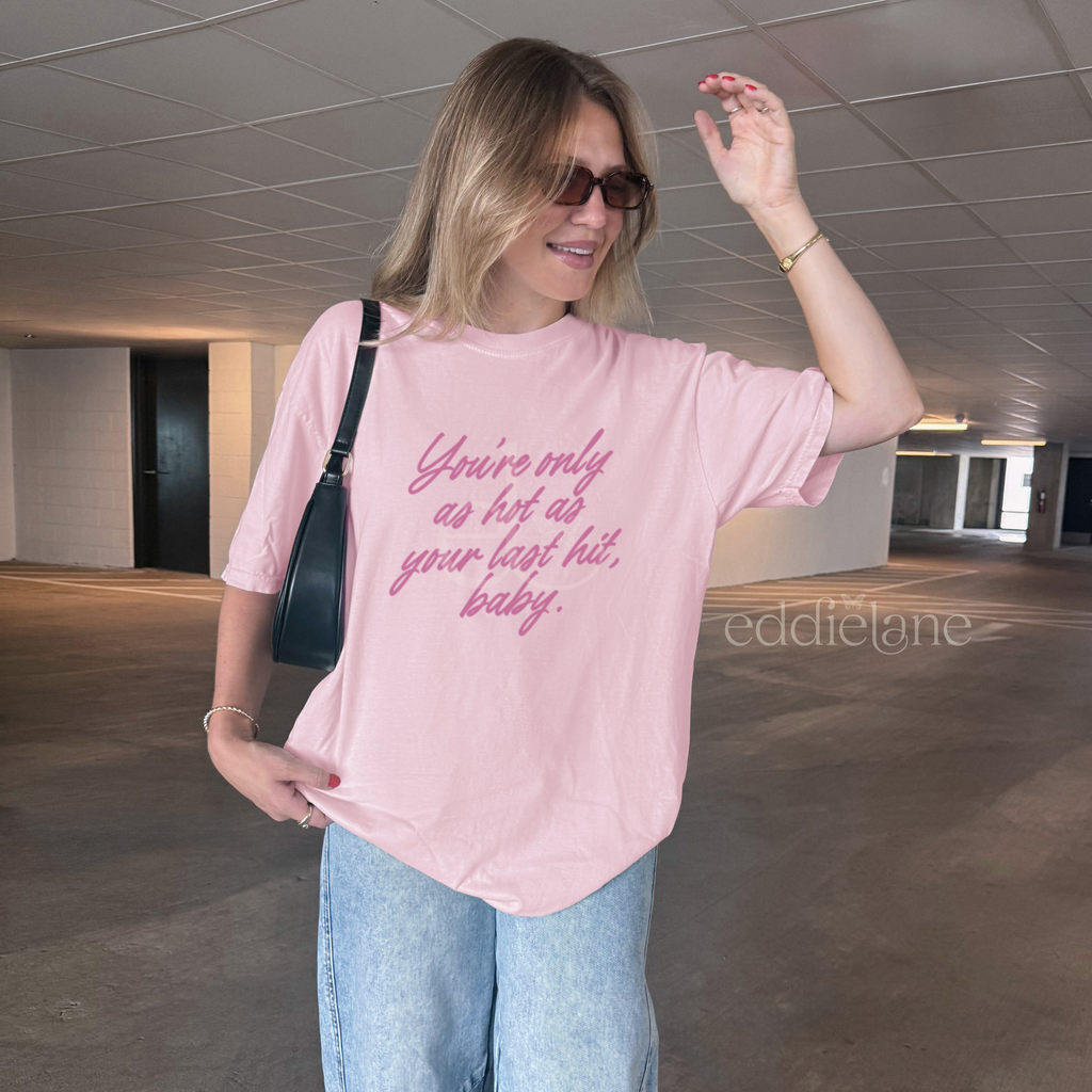 woman in a light pink comfort colors tee that says "you're only as hot as your last hit, baby" in pink.