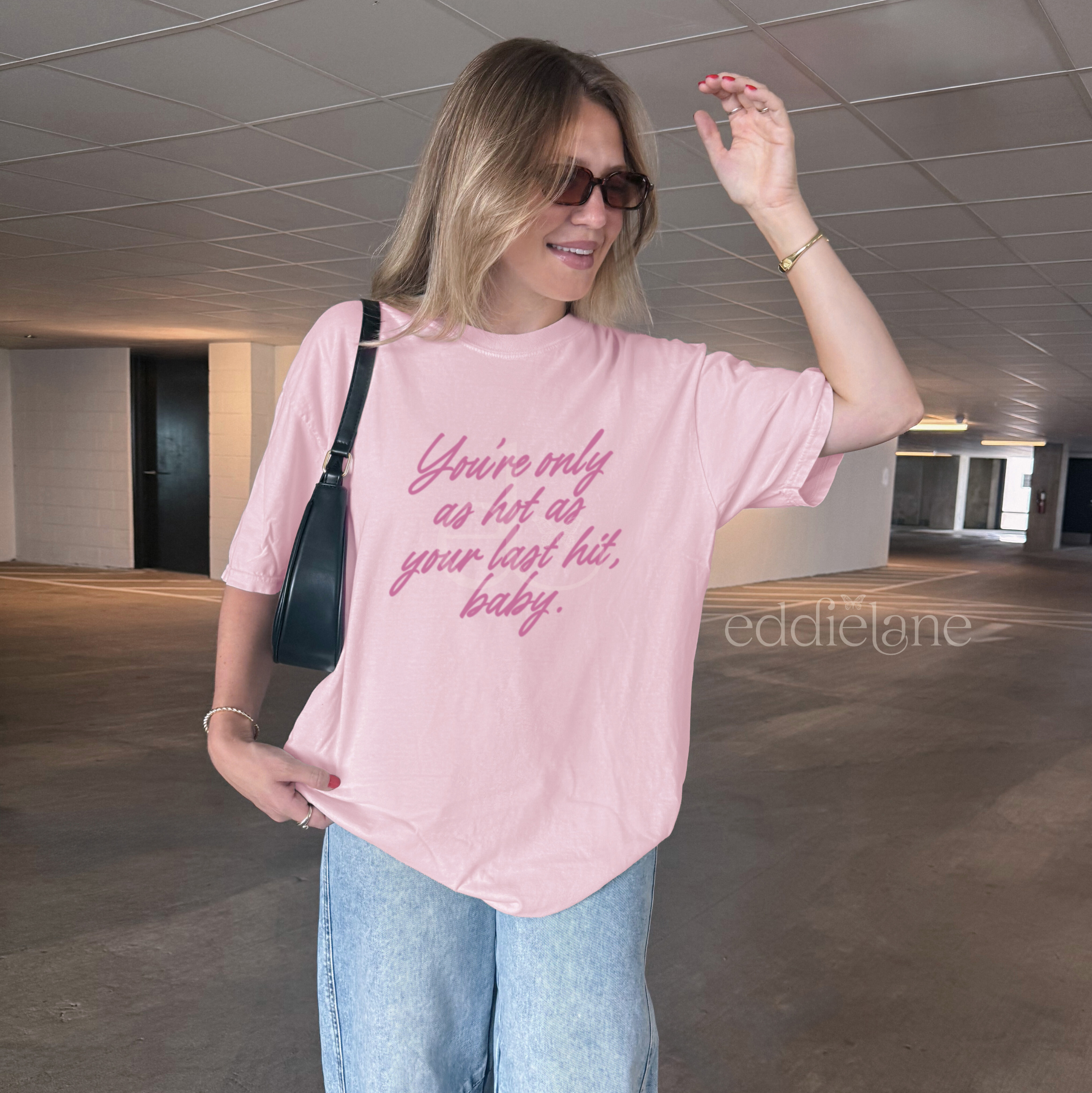 woman in a light pink comfort colors tee that says "you're only as hot as your last hit, baby" in pink.