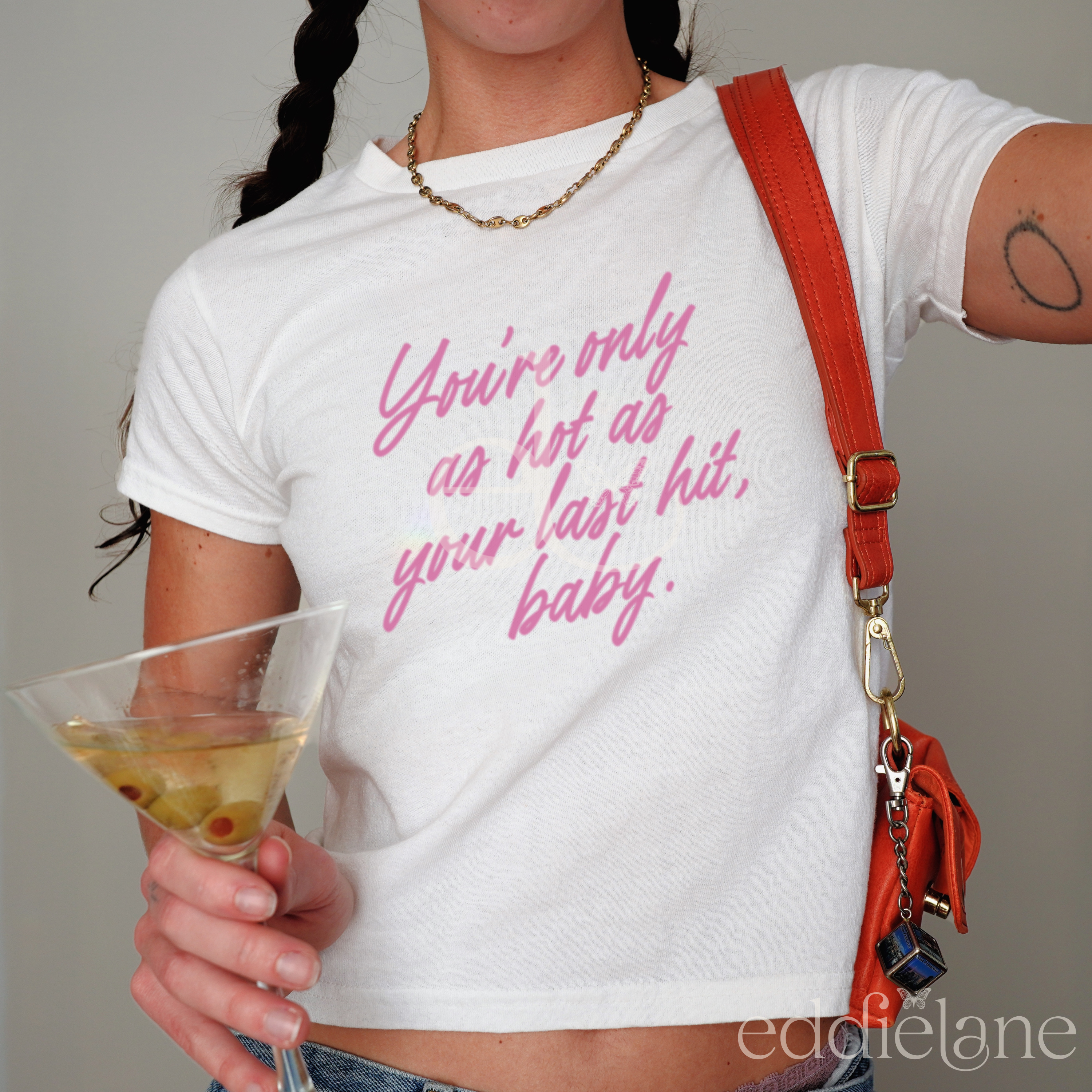woman in a white fitted baby tee that says "you're only as hot as your last hit, baby" in pink.