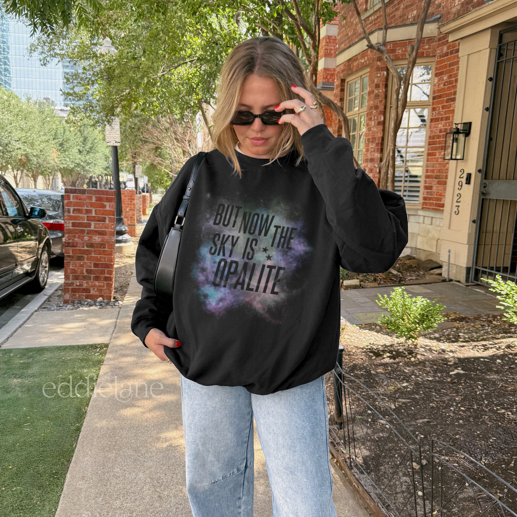 Woman wearing a black sweatshirt with the words "but now the sky is opalite" and a colorful galaxy design 