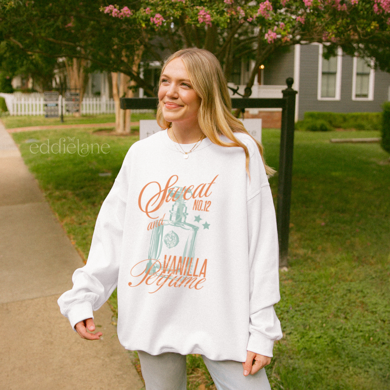 Woman wearing a white sweatshirt with a graphic of a perfume bottle and the words "sweat and vanilla perfume"