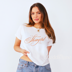 Woman wearing a white baby tee with cursive text that says 'Showgirl'