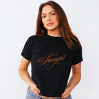 Woman wearing a black baby tee with cursive text that says 'Showgirl'