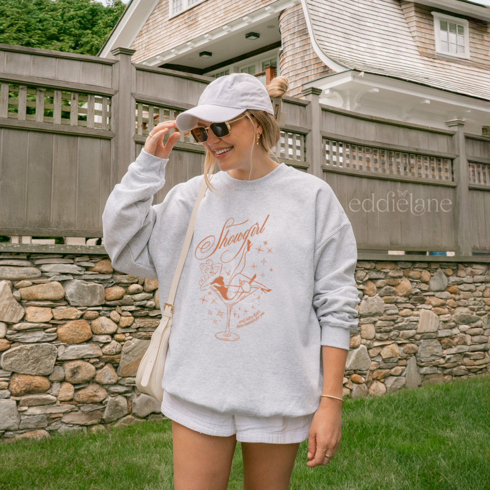 Woman wearing a gray sweatshirt with a graphic design featuring a woman in a martini glass and the word "showgirl"