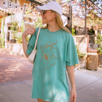Woman wearing an oversized green t-shirt with a graphic of a showgirl in a martini glass 