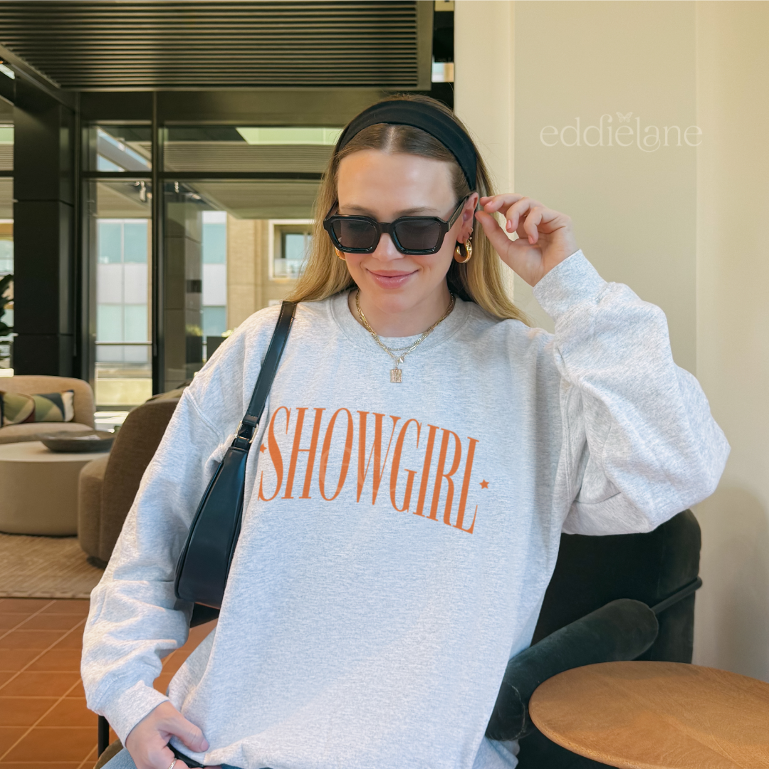 Woman wearing a 'SHOWGIRL' sweatshirt in an indoor setting